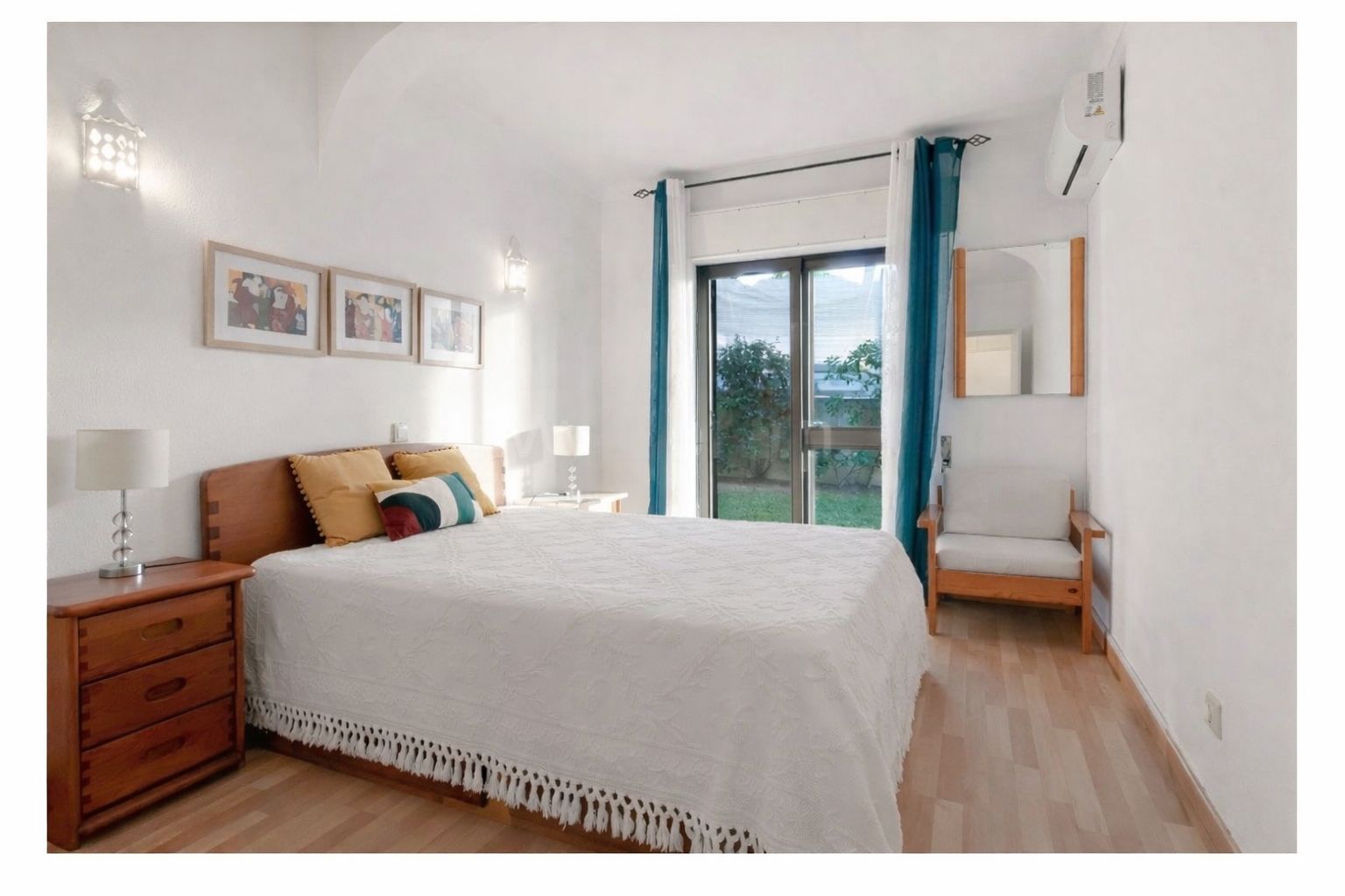 Main bedroom with a double bed, soft white linens, wooden side tables, and garden doors letting in morning light