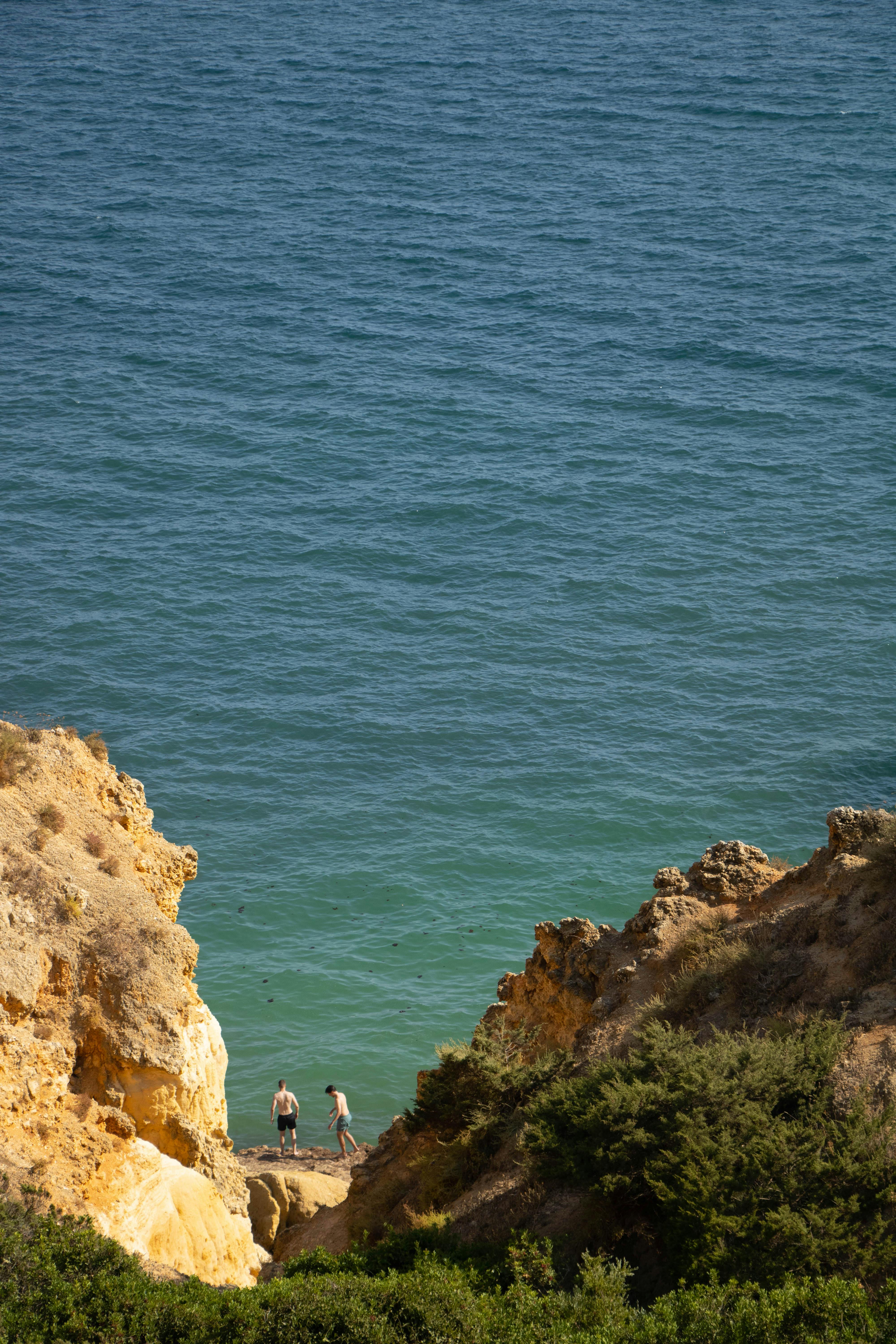 Turquoise cove with ochre cliffs and two swimmers at the water edge